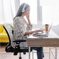 Woman working at desk with laptop, wearing white headphones, seated in ergonomic office chair, home office setup